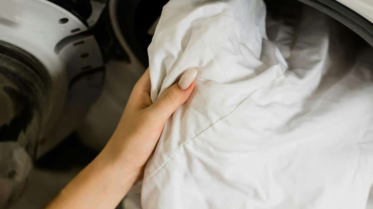 A person's hand holding white laundry in front of a washing machine.
