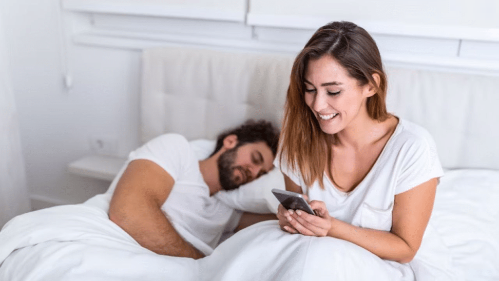 Man sleeping as his partner scrolls on her phone in the background