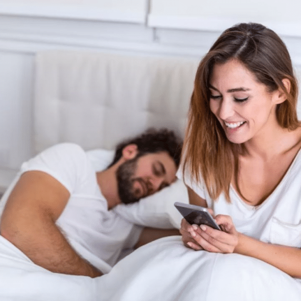 Man sleeping as his partner scrolls on her phone in the background