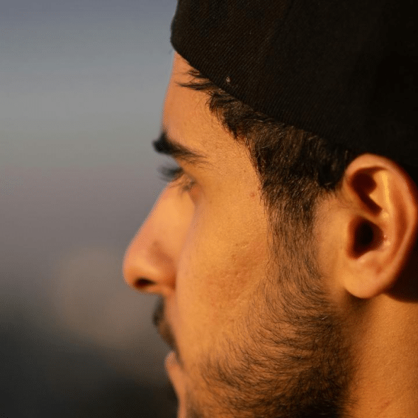 A close-up side profile of a man wearing a black cap.