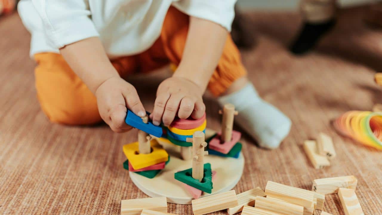 A child playing with colorful wooden stacking toys on the floor.
