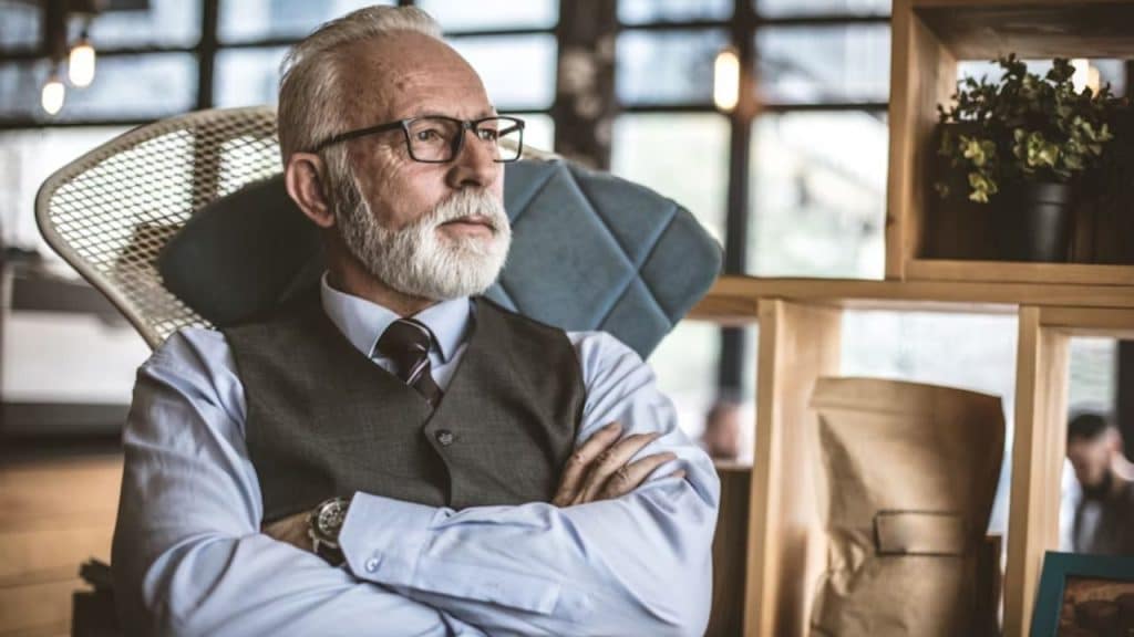 An older man sitting alone in the living room looking thoughtful.