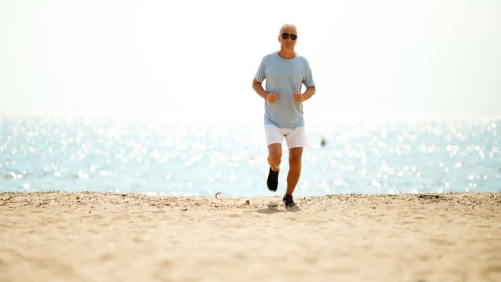 An older man walking alone on the beach for exercise