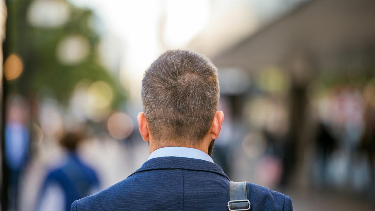 A man wearing a suit walking in the city with his back to the camera.