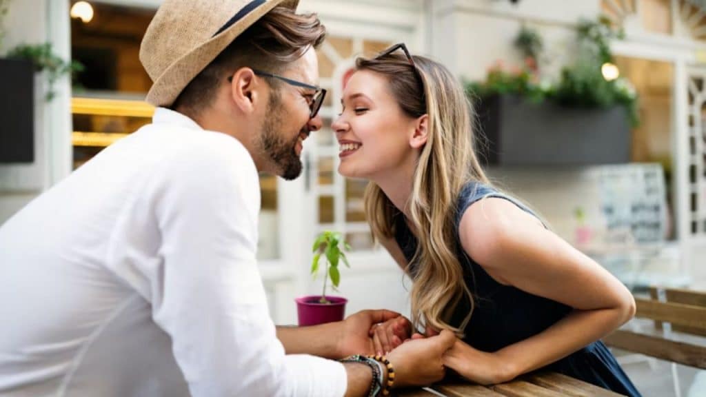 A thoughtful man smiling warmly while holding the hands of a happy woman