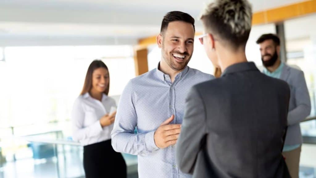 A man confidently speaking in a small meeting while his partner supports him
