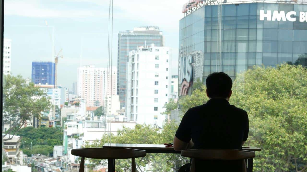 A man sitting alone at a table looking out at the city through a large window.