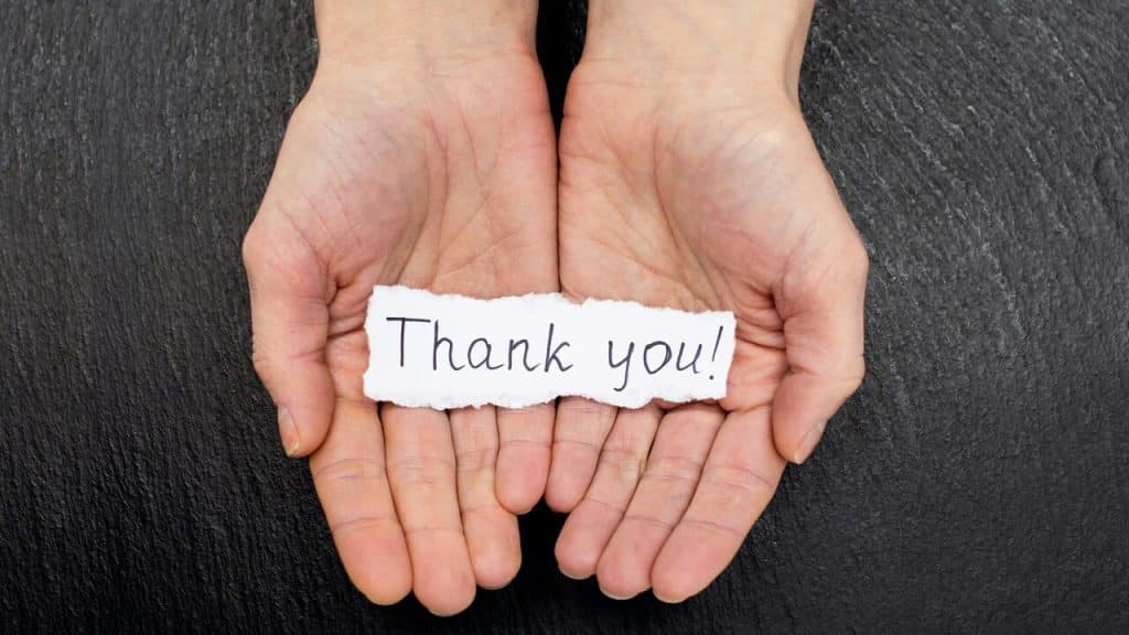 A hand holding a handwritten note saying “thank you”