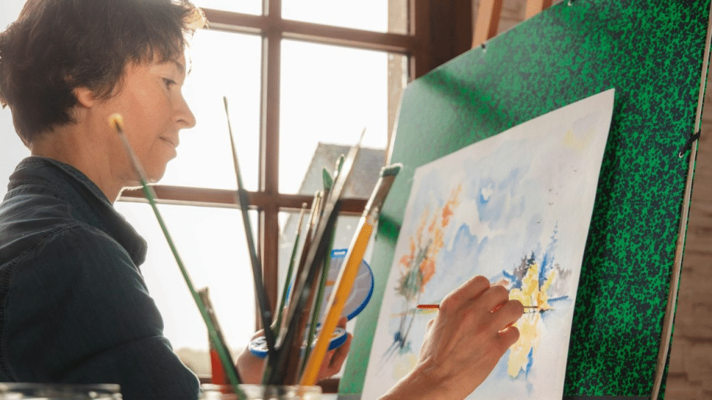 A person with short brown hair paints a landscape on an easel.