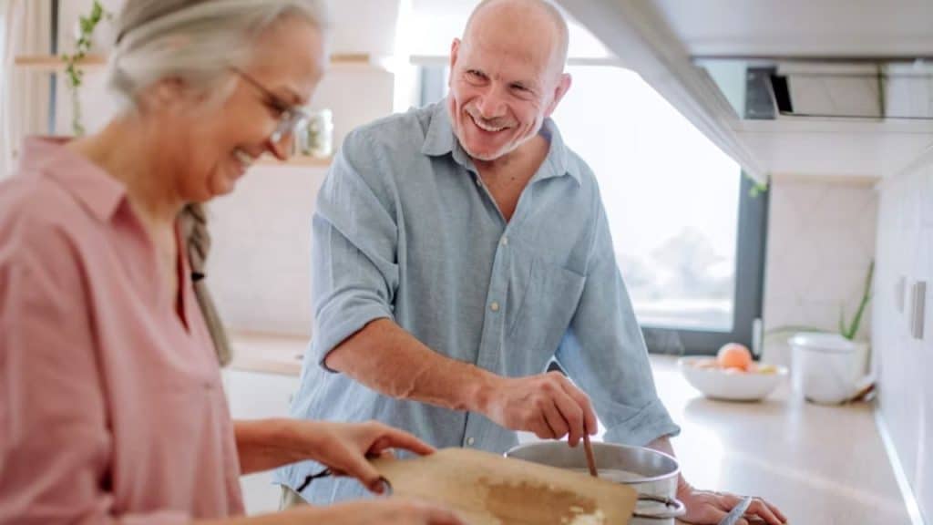 A man cooking while his wife helps