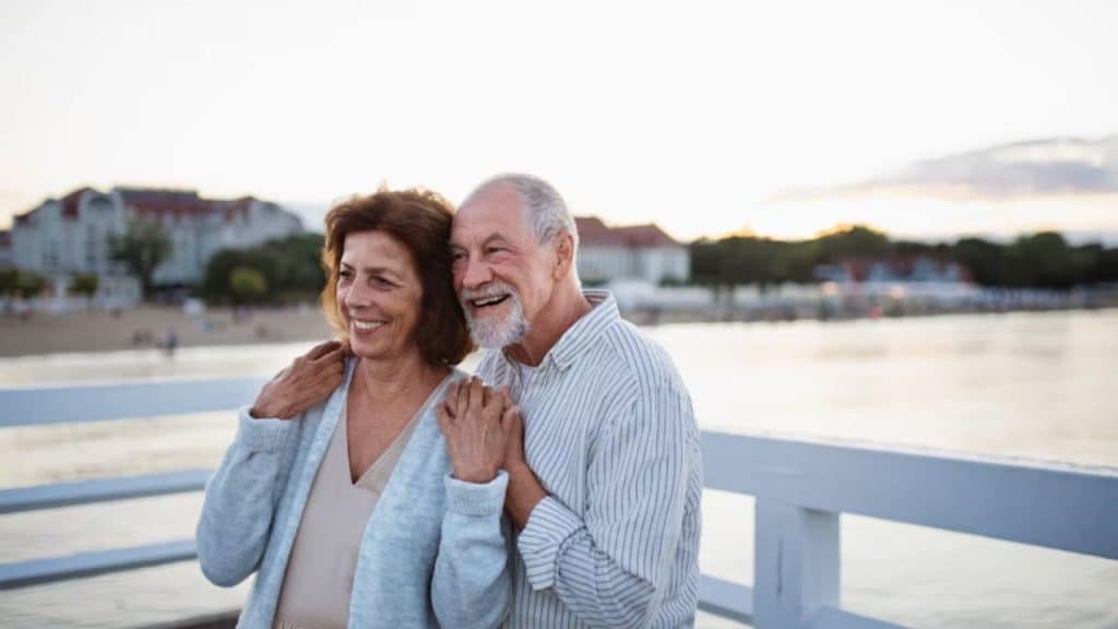 An older couple holding hands while watching the sunset