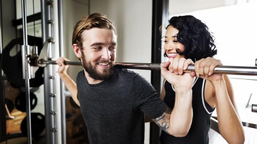 Man lifting weights while woman supports him with a smile