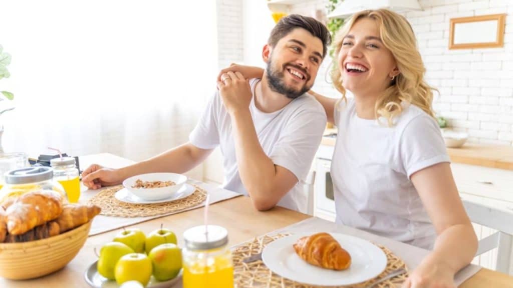  A couple laughing while having breakfast together.