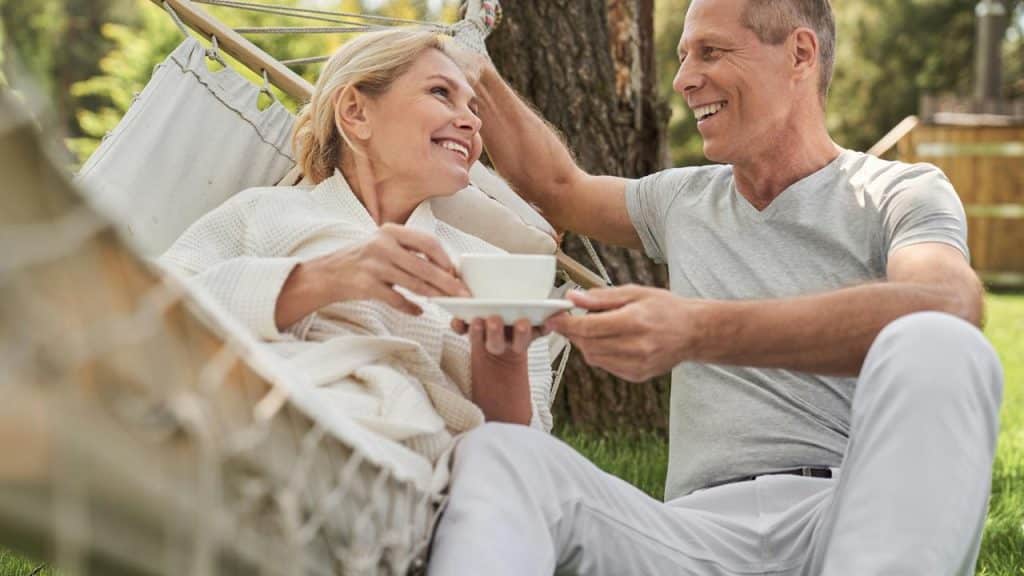 A smiling couple relaxing outdoors with a cup of coffee in a hammock.