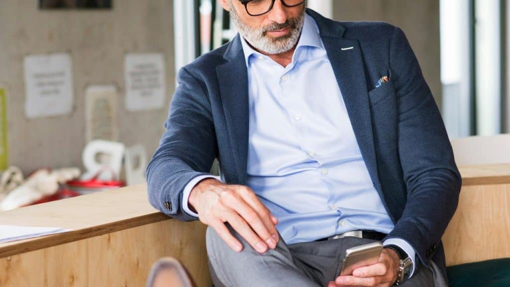 A man in a suit sitting and looking at his smartphone.