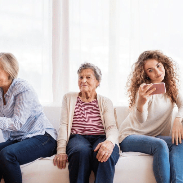 A grandmother, mother, and granddaughter sit on a couch using their phones.