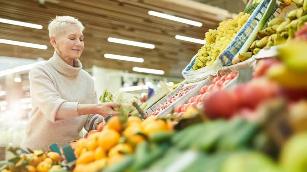 A woman choosing fresh vegetables in a grocery store produce section.