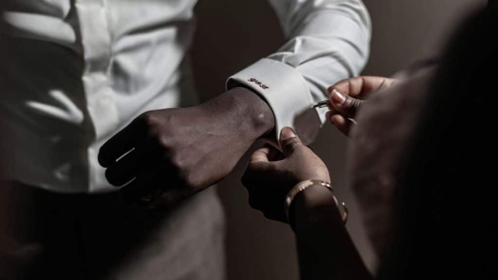 A person fastening cufflinks on the sleeve of a white dress shirt.