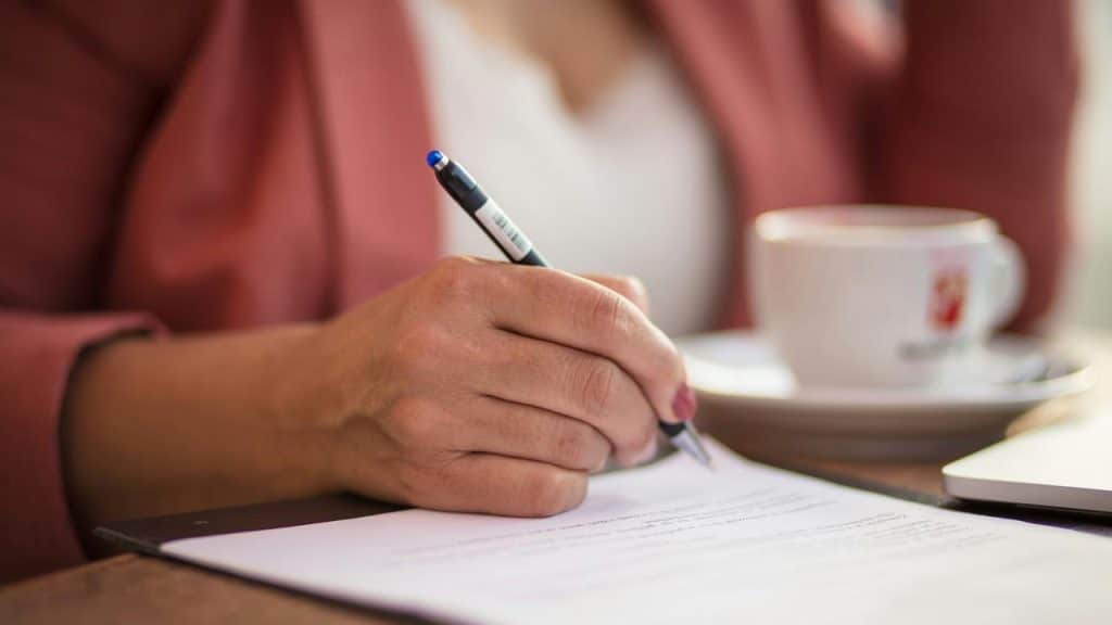 A person writing on a document with a pen at a desk.