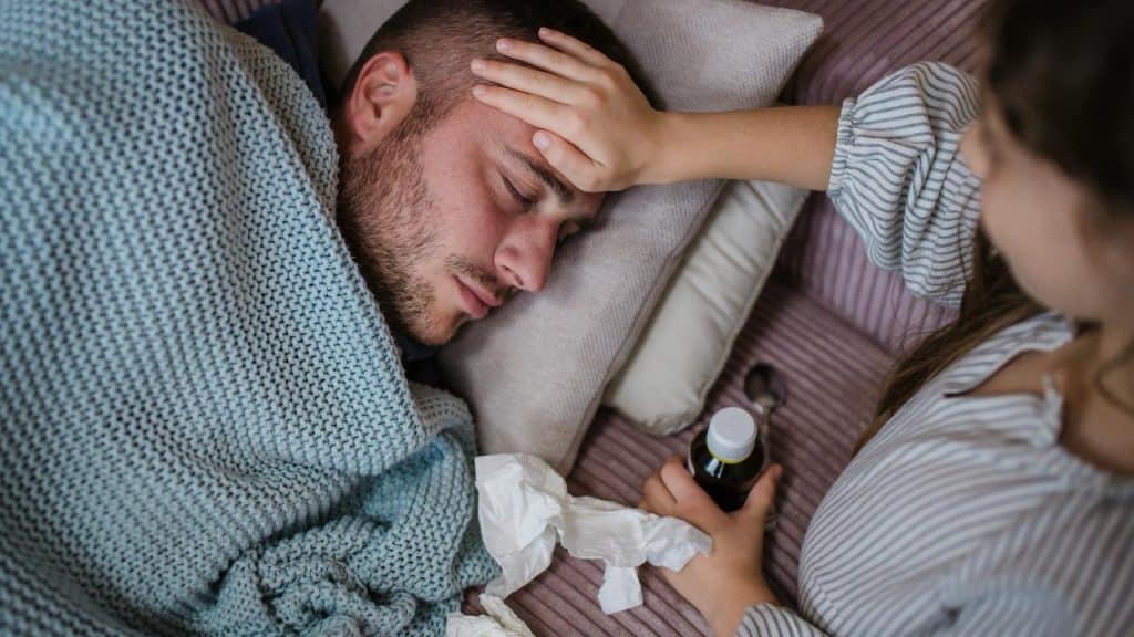 A woman caring for a sick man lying in bed under a blanket.