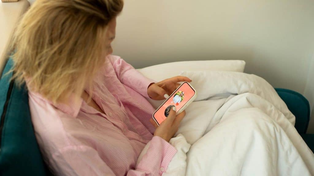 A person in pink pajamas looking at a phone while lying in bed.