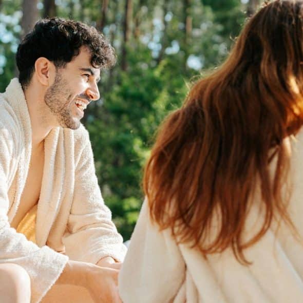 A man and woman in bathrobes talking by a pool.