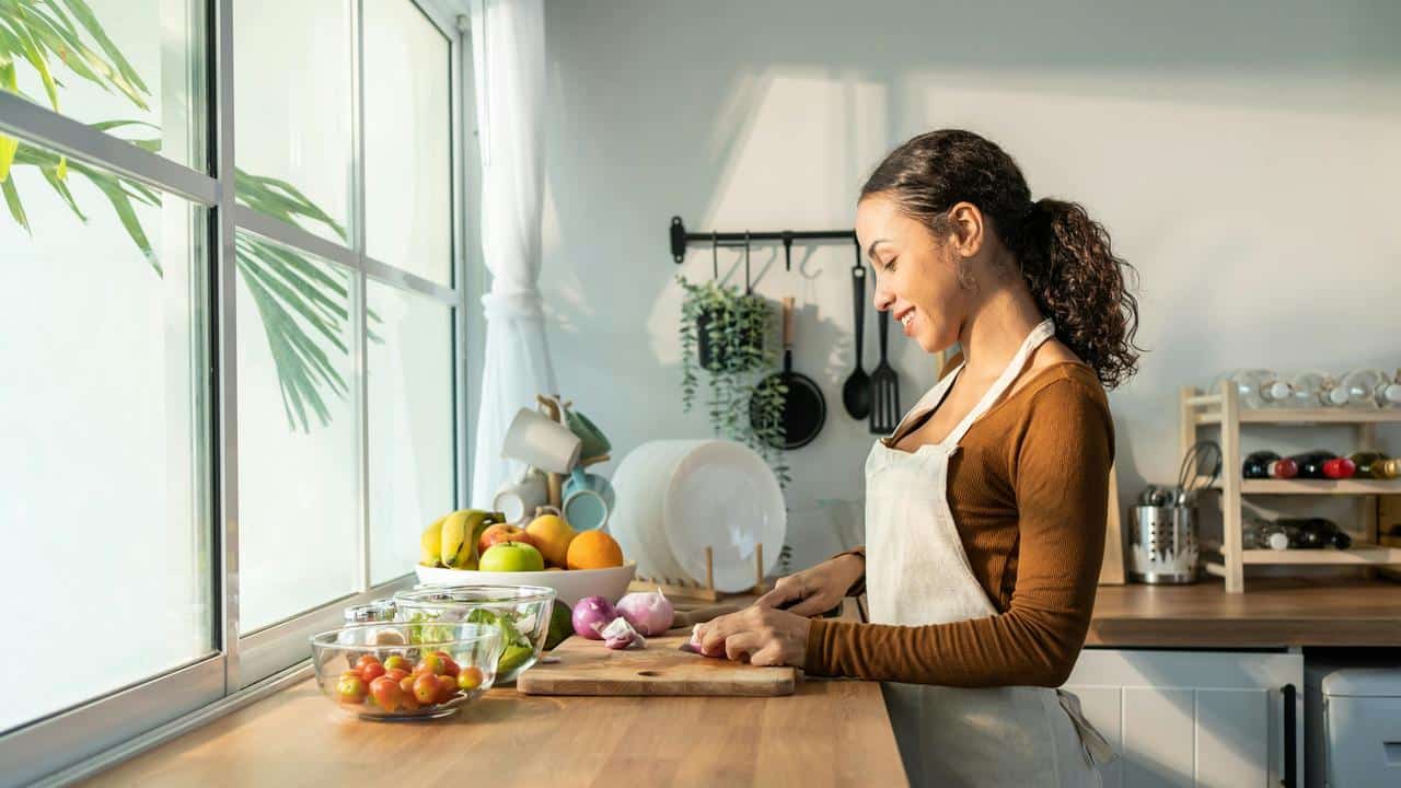 A woman in an apron chopping vegetables in a bright kitchen.