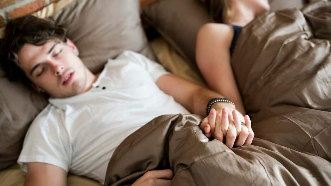 A couple sleeping in bed while holding hands.