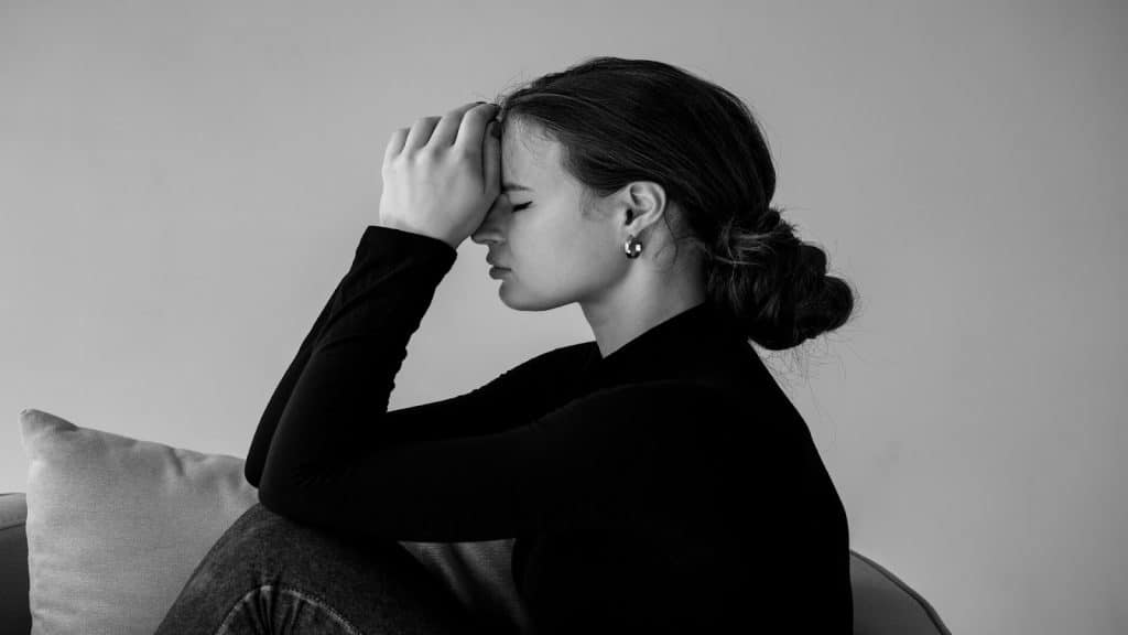 A young woman with her eyes closed and hands on her head, looking pensive.