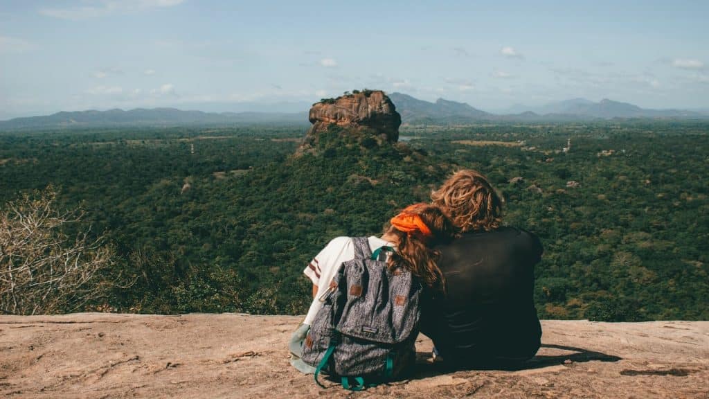 A man and a woman sitting on a rock, looking at a mountain formation in the distance.
