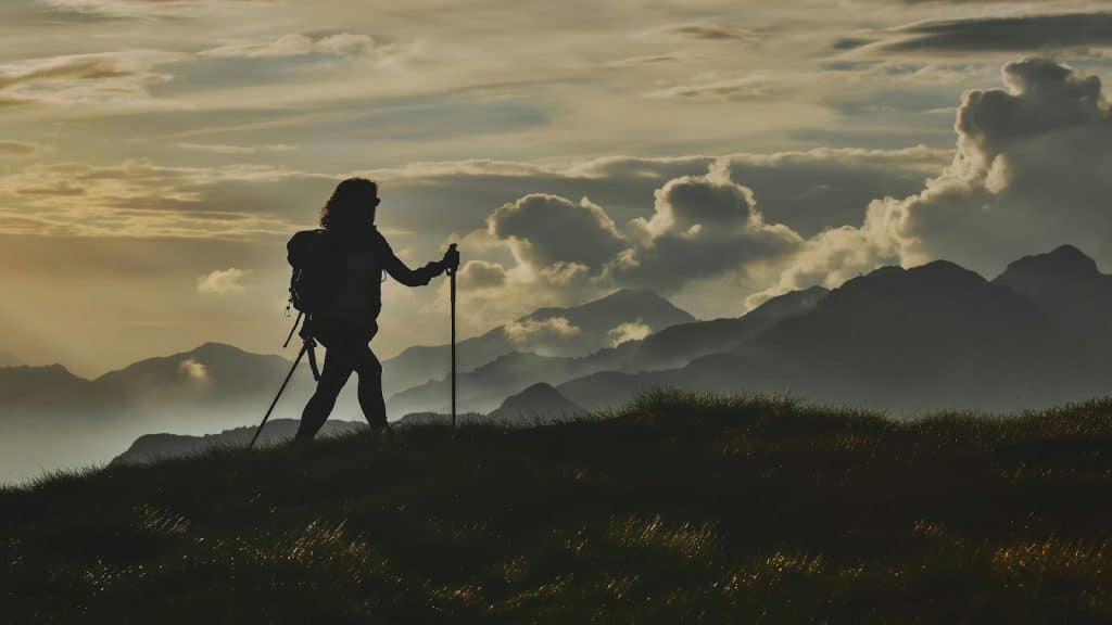 A person hiking in the mountains, silhouetted against a cloudy sky.