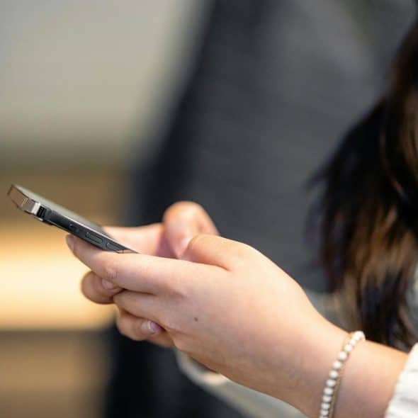 A person holding a smartphone while wearing a white sweater.