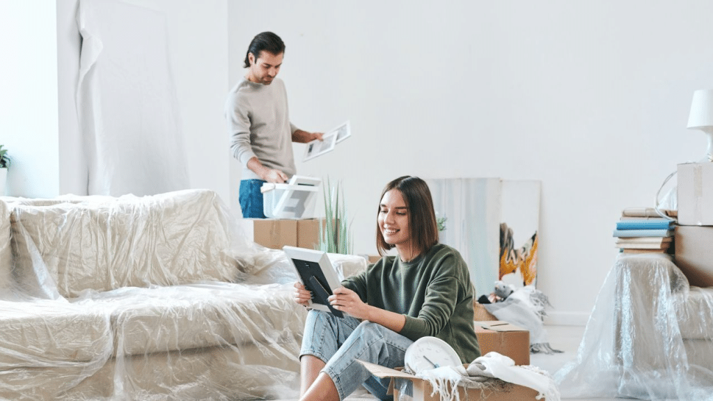 A man unpacking boxes, with the woman looking at a framed photo.