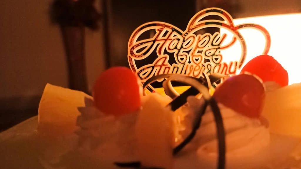 A close-up of an anniversary cake with fruit and a “Happy Anniversary” topper.