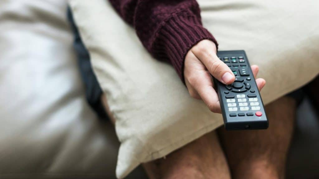 A person holding a TV remote while sitting on a couch.