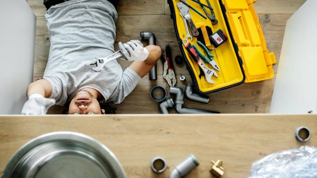 A person lying under a sink with tools, working on plumbing repairs.