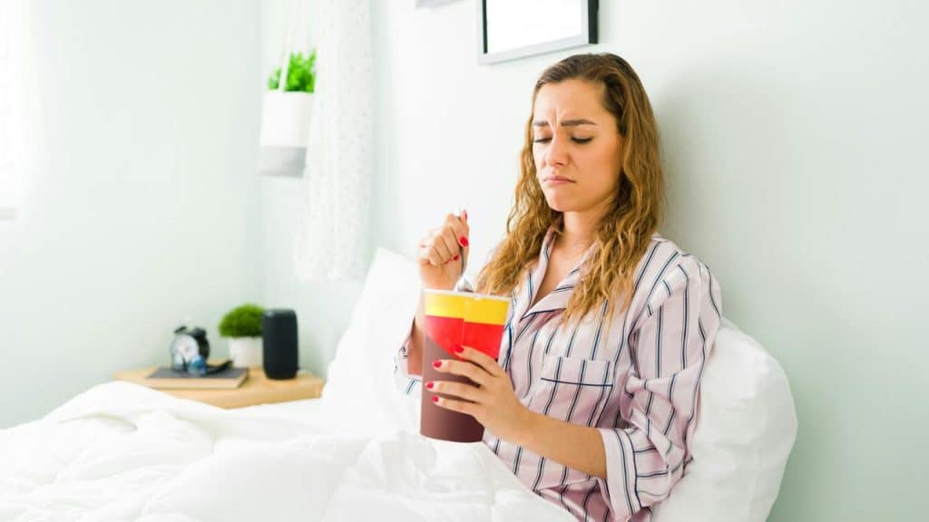 A woman in bed holding a bucket of ice cream.