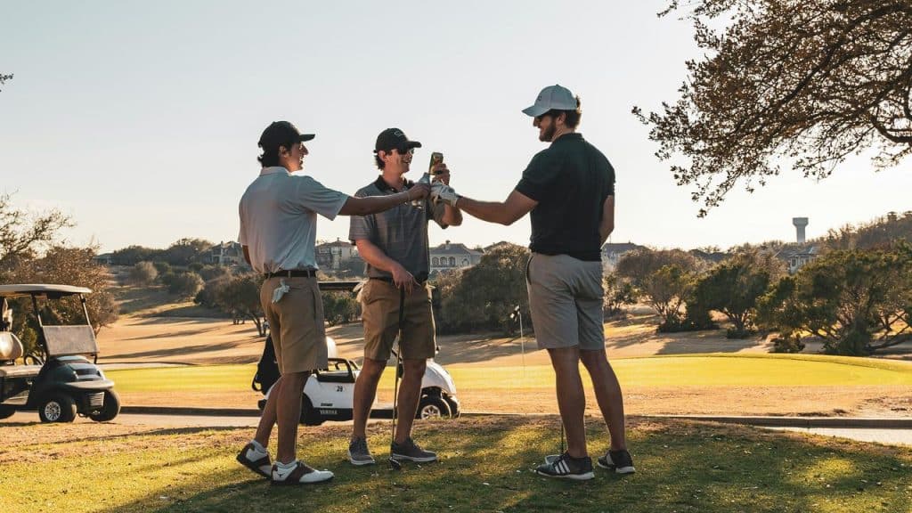 A trio of men on a golf course toasting with drinks.