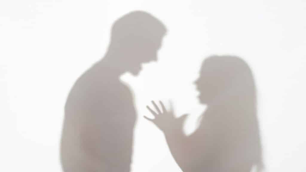Silhouettes of a man shouting at a woman with an open mouth and raised hand.