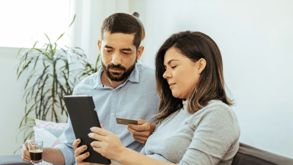 A concerned man holds a credit card while looking at a tablet with a woman.