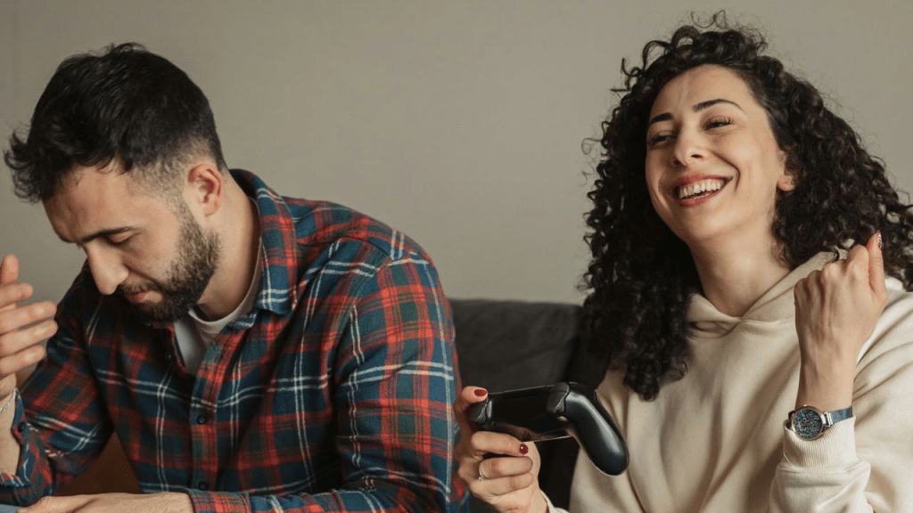 A man looks disappointed while a woman laughs and plays a video game.