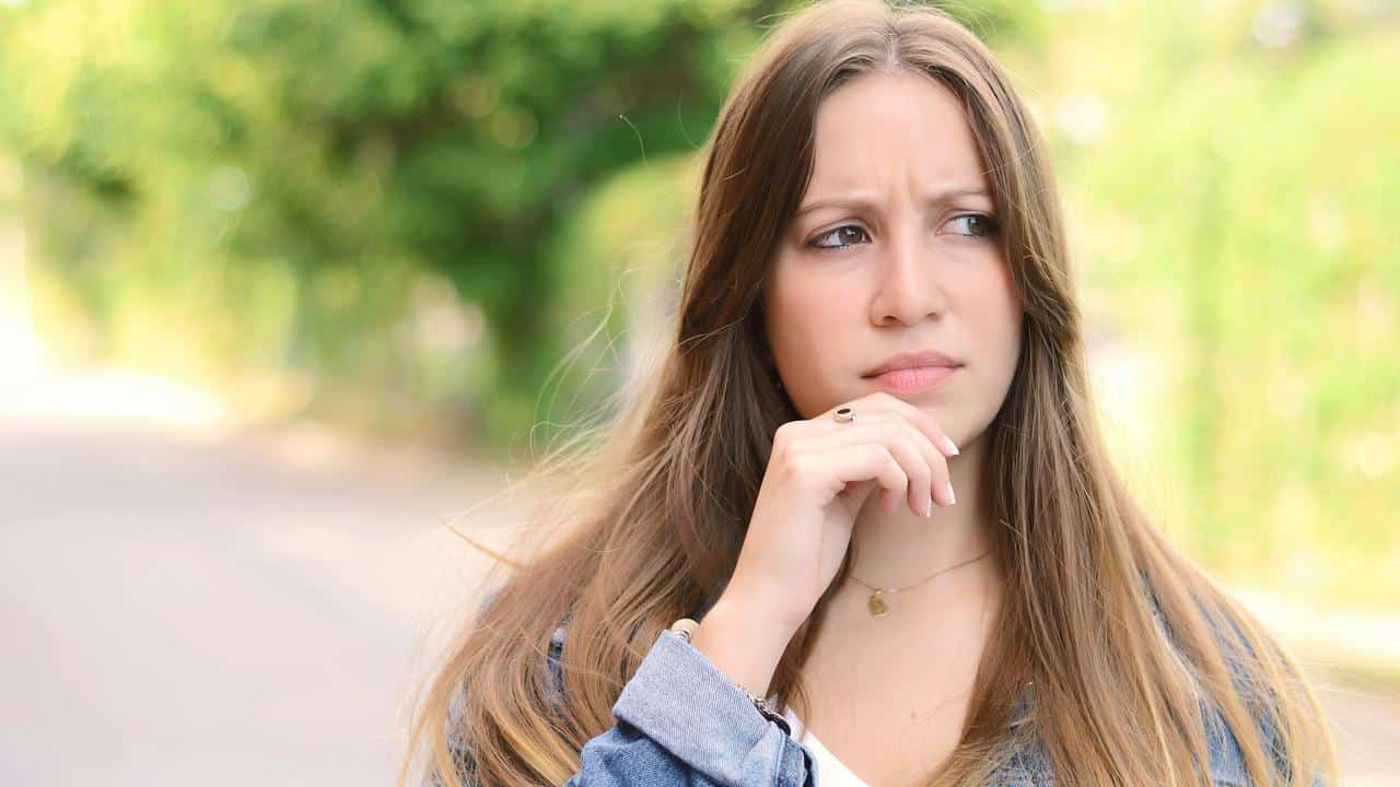 A young woman outdoors looking thoughtful with her hand on her chin.