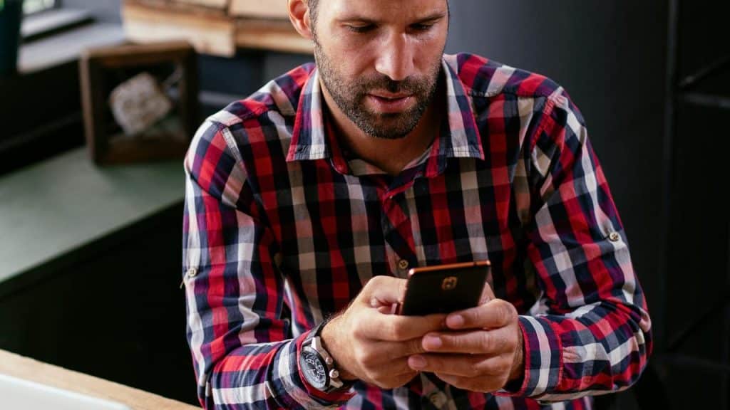 A man in a plaid shirt looking at his phone indoors.