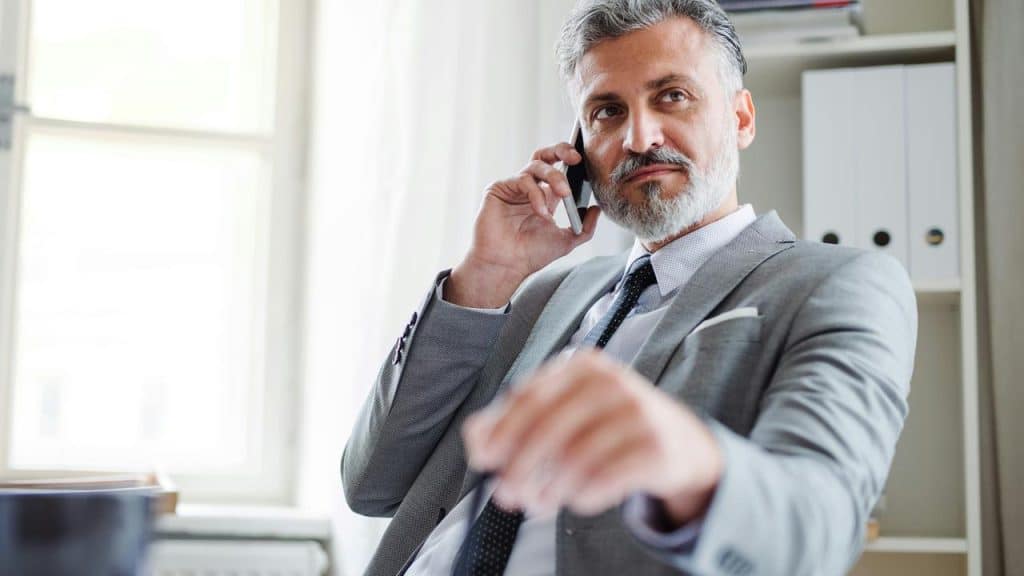 A mature man in a suit talking on his phone in an office.