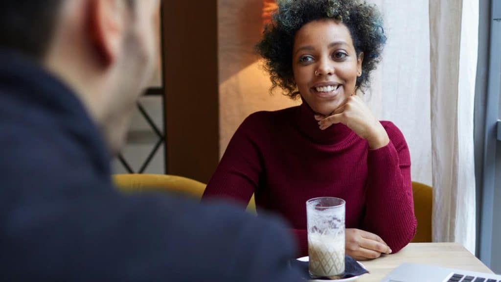 A woman in a red sweater smiling during a conversation at a café.