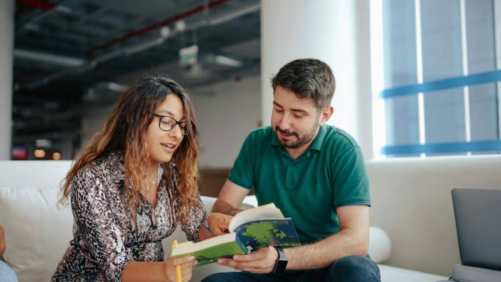 A man and woman sitting together reading a book indoors.