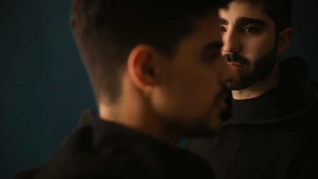 A man in focus staring forward while another man is blurred in the foreground.