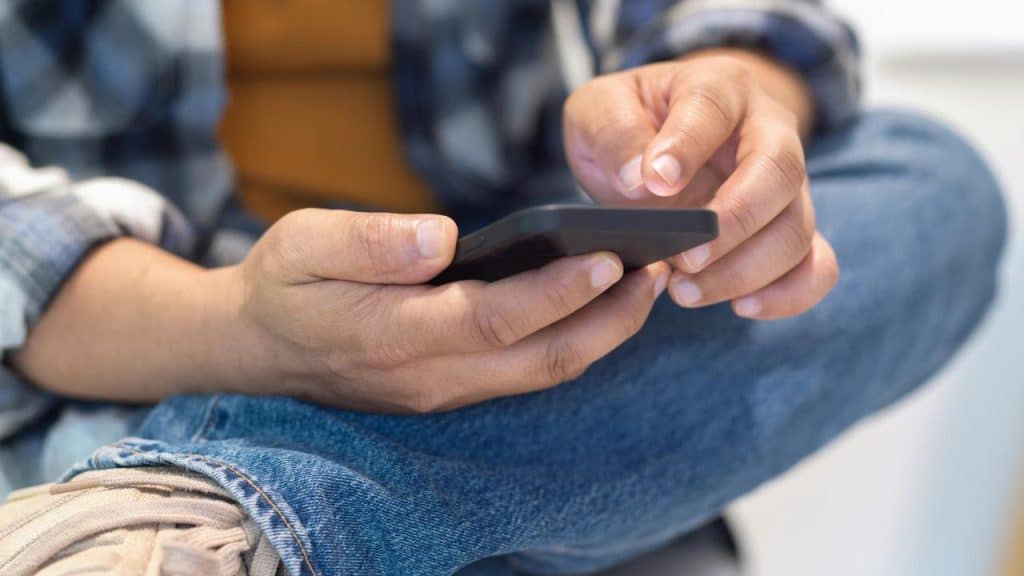A person holding a smartphone and using it while sitting cross-legged.