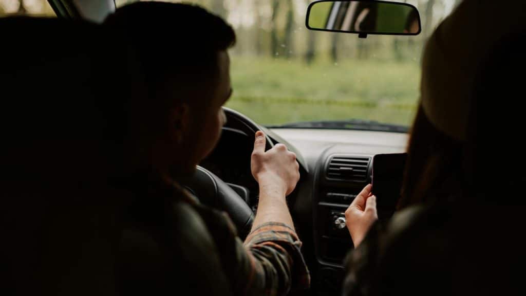 A man driving a car while a passenger holds a smartphone.