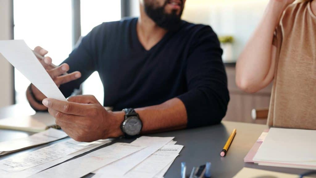 A man holding papers while discussing finances at a table with another person.